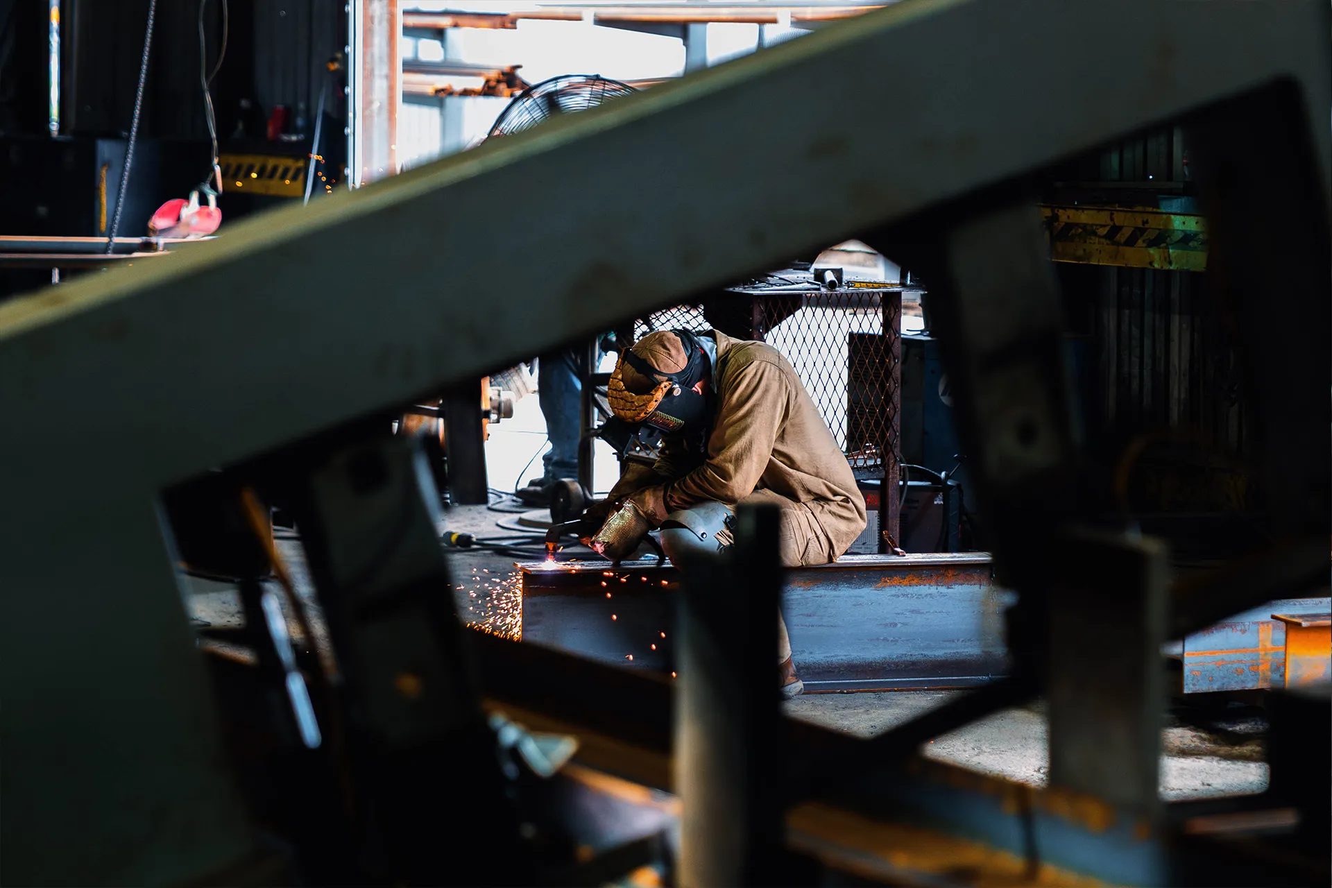 Welder fabricating steel beam on manufacturing shop floor